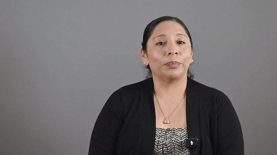 Judith Cortes in a black cardigan, looking up thoughtfully, a frame from the film Answer the Email